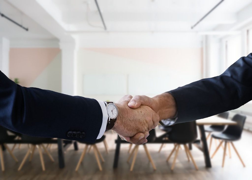 Two individuals in business attire shaking hands, with a focus on the handshake, symbolizing agreement, partnership, or conclusion of a deal in a professional setting.
