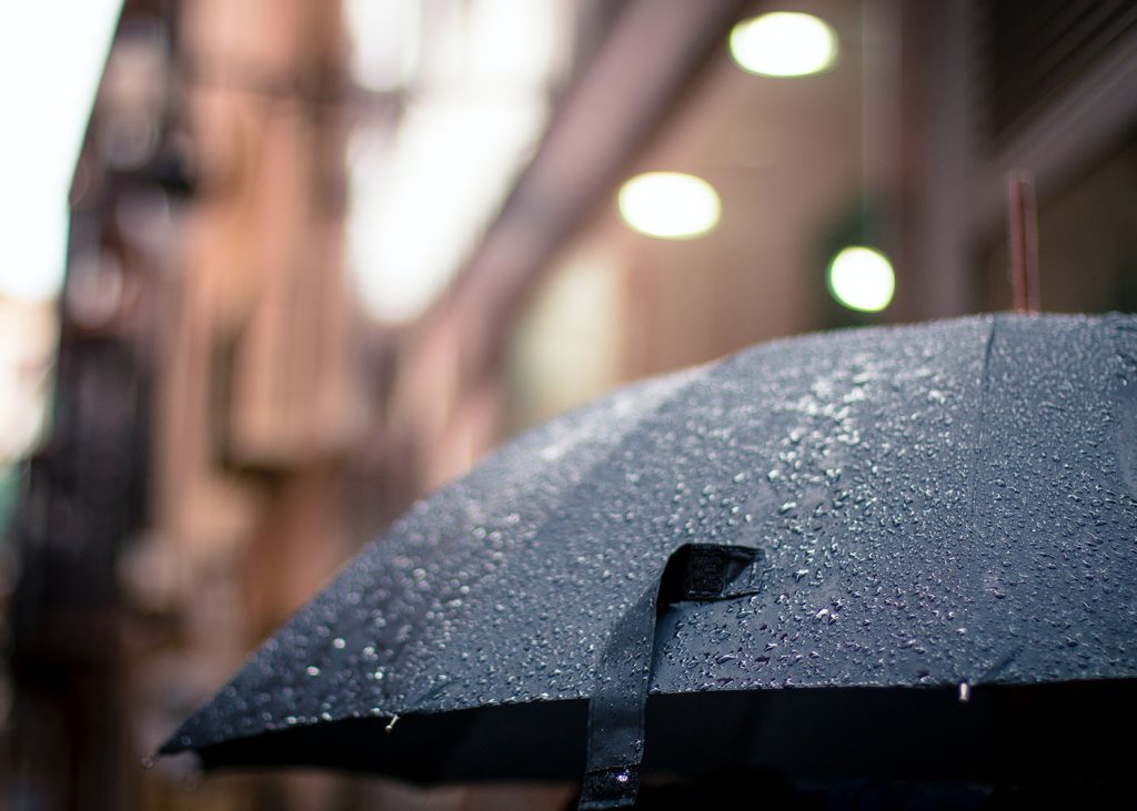 A person holding an umbrella in the rain, seeking shelter from the downpour.