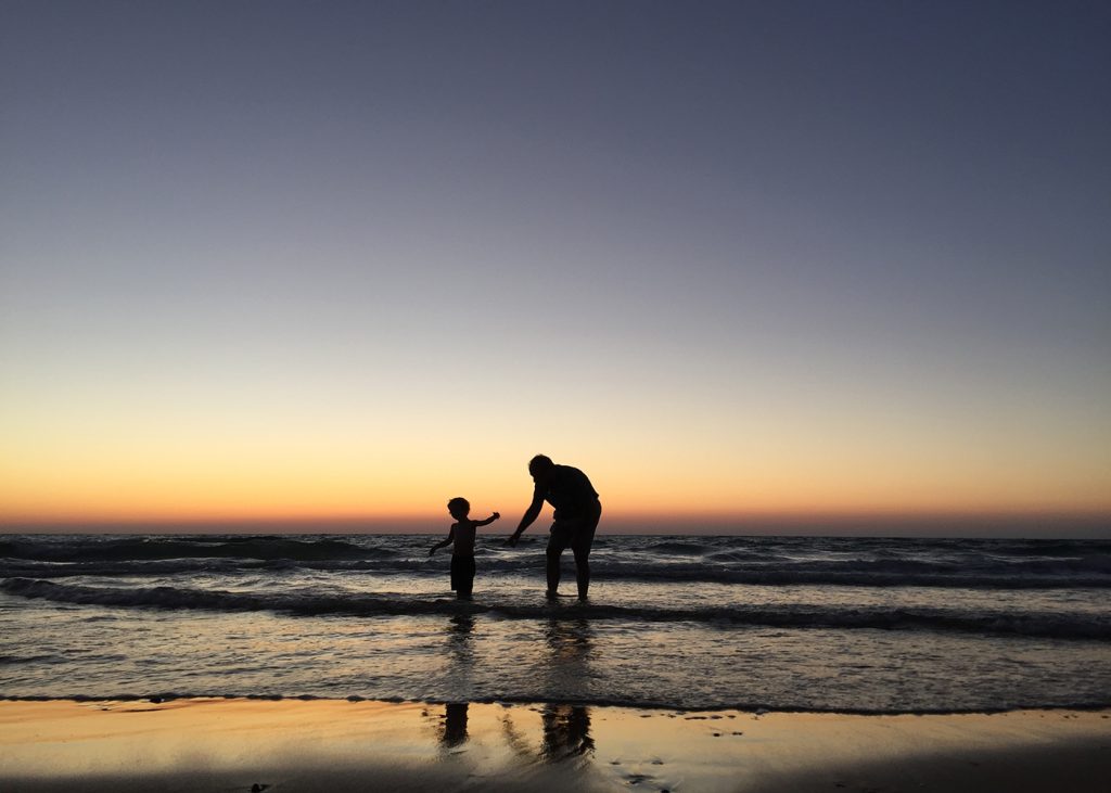 Father and son enjoying a beautiful sunset on the beach, creating lasting memories together.