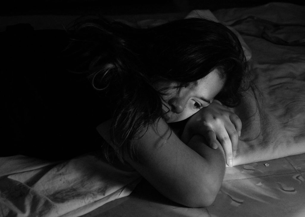 Image of a woman reclining on a bed in a dark setting.