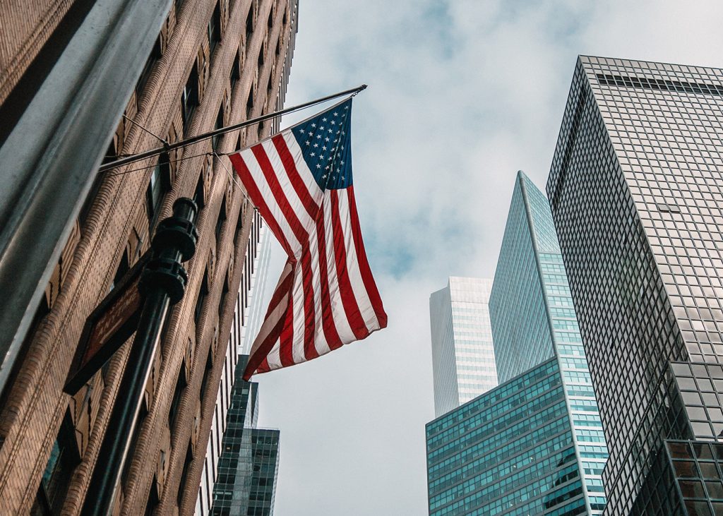 An American flag waving in front of towering buildings, symbolizing patriotism and national pride.