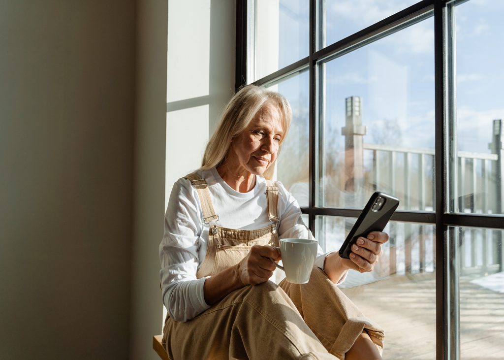 Elderly woman with coffee mug looking at smartphone screen.