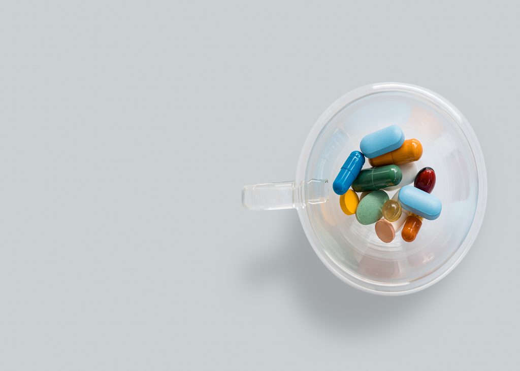 A plastic cup filled with pills on a gray background.